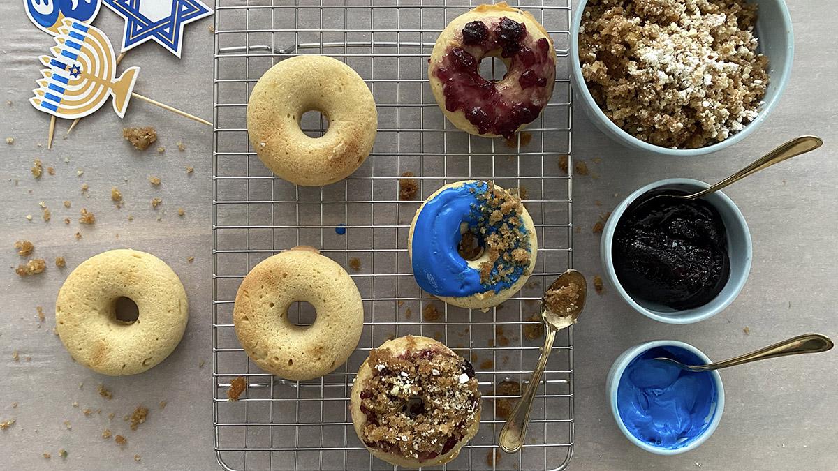 Assorted freshly baked donuts on a wire rack being frosted and covered with toppings