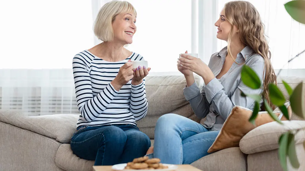 Photo of two women drinking coffee,  eating cookies, and offering words of encouragement to each other.