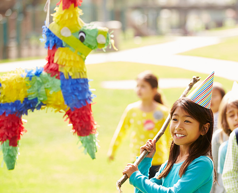 a photo of birthday traditions: girl hitting a pinata